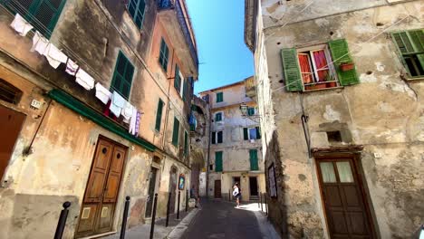 Der-Pov-Einer-Person,-Die-In-Der-Schmalen-Straße-Von-Ventimiglia-Spazieren-Geht,-Während-Kleidung-Zum-Trocknen-An-Den-Gebäuden-Hängt