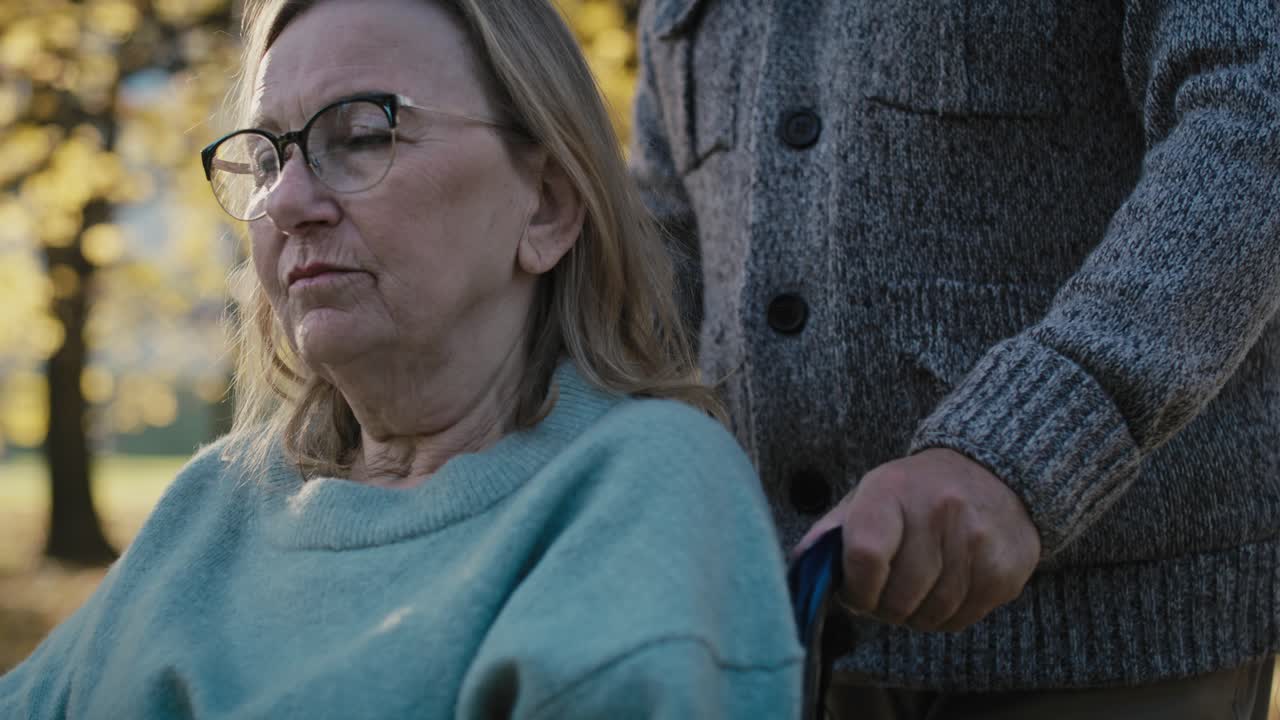 primer plano de un hombre mayor empujando a una mujer en silla de ruedas en el parque