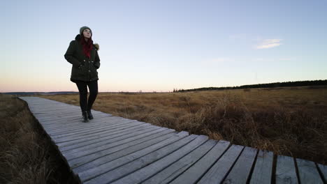Beautiful-woman-walking-on-wooden-pathway-in-natural-marshland,-slow-motion