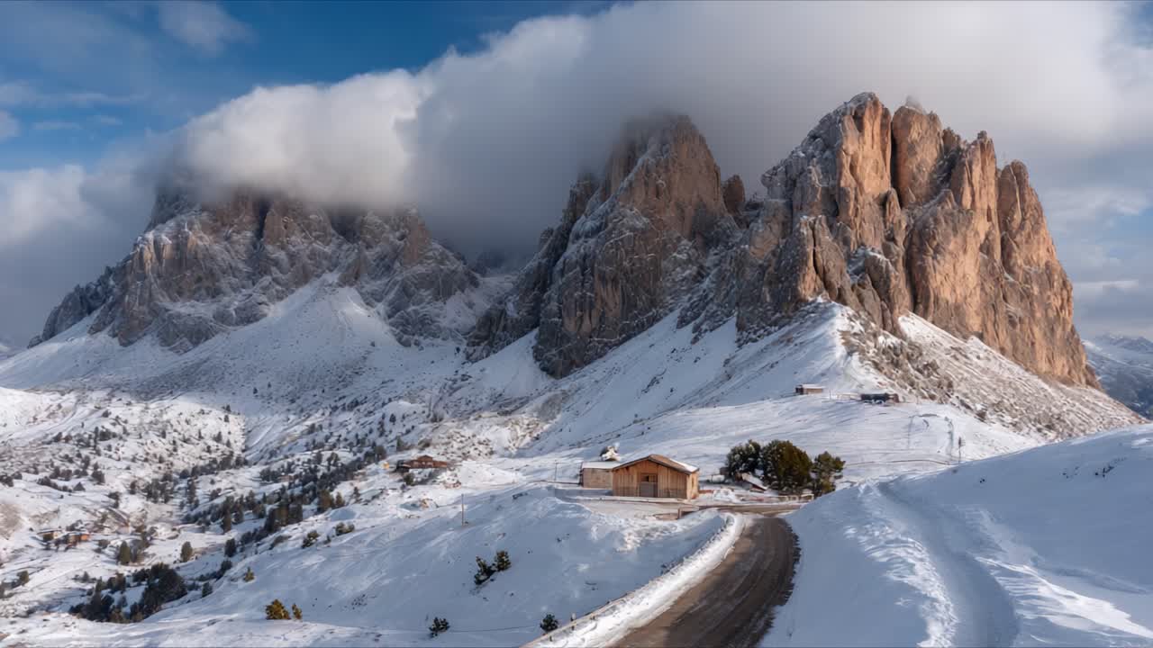 A Stunning Alpine Landscape Featuring Snow-Covered Mountains, Rolling Hills, and a Peaceful Cabin Under a Cloudy Sky – Exploring Nature's Breathtaking Beauty