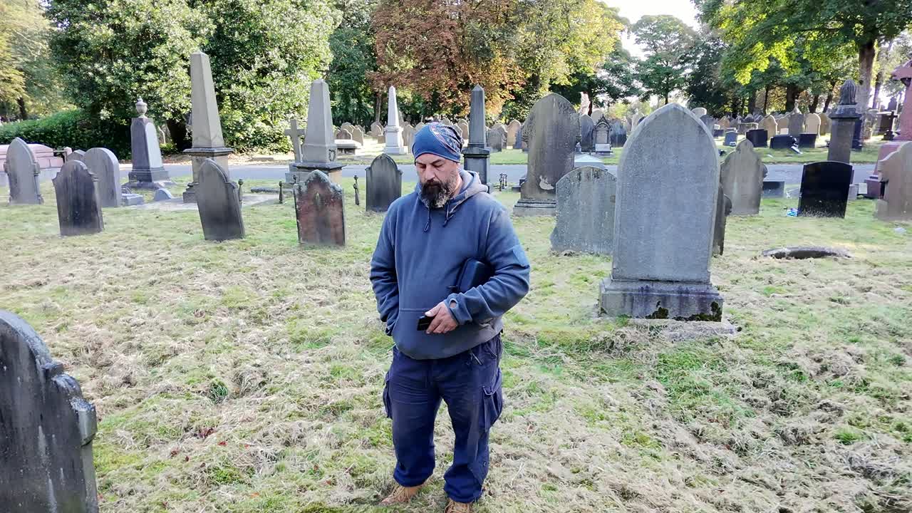 Following male wearing hat mourning loss in peaceful sunlit cemetery rising aerial view