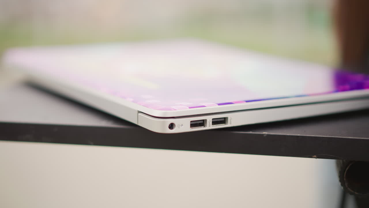 DJ afroamericano che collega il laptop su un tavolo, le mani inseriscono un cavo intrecciato rosso in un sottile laptop argentato che mostra una forma d'onda viola, setup focalizzato per performance di strada, sfondo di parco urbano, primo piano con bokeh morbido.