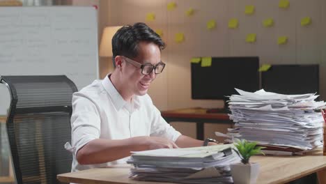 hombre asiático feliz celebrando el final de trabajar con documentos en la oficina