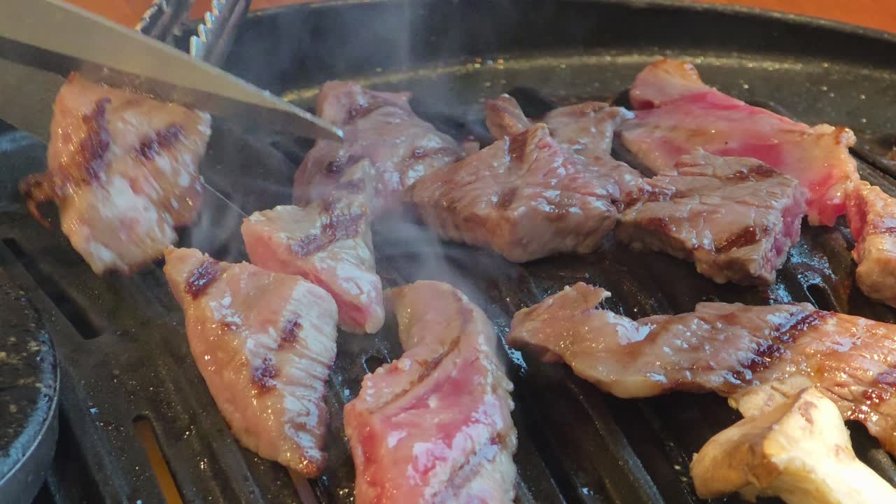 Sizzling pieces of beef being grilled and cut with scissors on a hot plate at a Korean BBQ restaurant - close-up