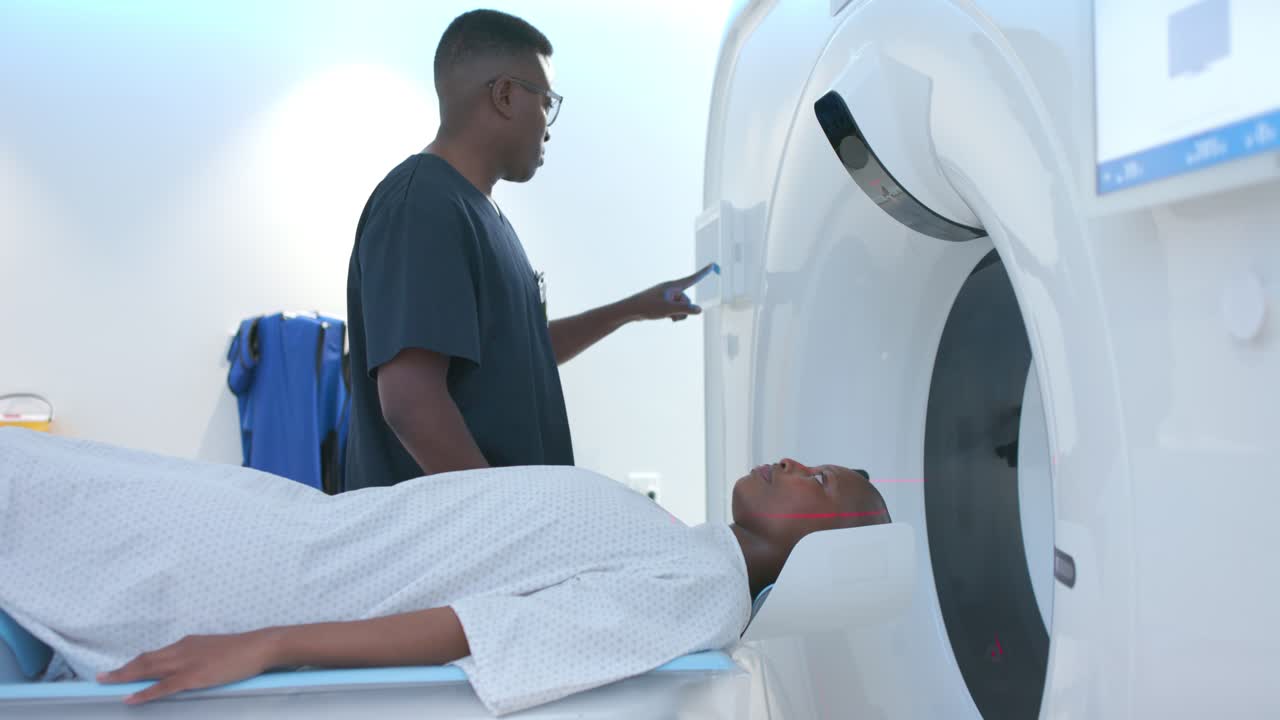 Tecnico africano che modifica la posizione della testa di un paziente sul tavolo della TAC, dopo l'allineamento laser, premendo il gantry per la TAC