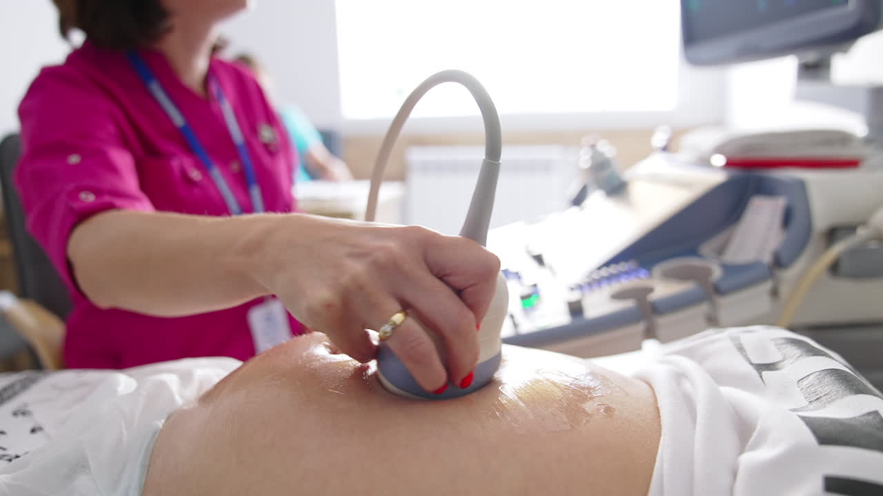 Female doctor examining belly of pregnant woman with ultrasound. Gynecologist moving transducer on abdomen of a future mother in clinic during ultrasonography process.