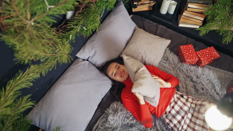 cute woman throws pillow to the air laying on bed. room decorated before christmas. video from the top.