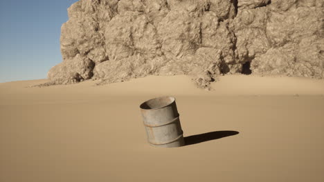 a rusty barrel sits in the desert sand with a large cliff in the background