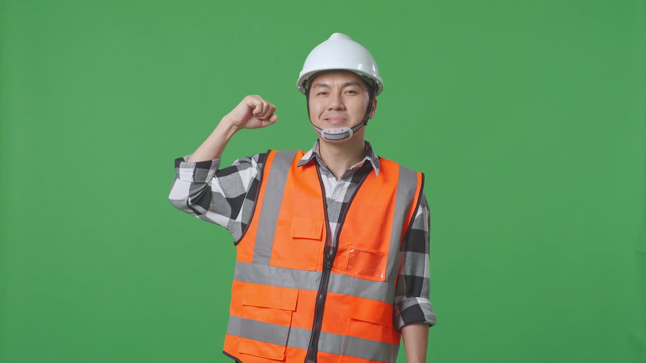 Asian Male Engineer With Safety Helmet Flexing His Bicep And Smiling To Camera While Standing In The Green Screen Background Studio