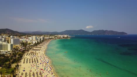 Cala-major-beach-with-turquoise-waters-and-crowded-sandy-shore,-sunny-day,-aerial-view