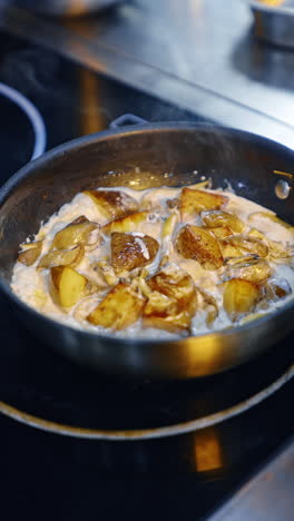 potato pieces cooked in white sauce in the frying pan. dark sauce is added to the dish. close up. vertical video.