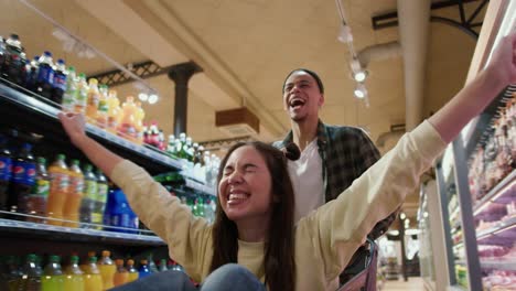 close up of a young couple having fun, man pushing shopping cart with his girlfriend inside