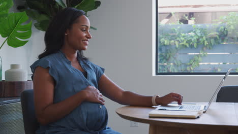 pregnant african american woman using laptop at table working from home
