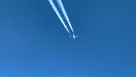 pilot pov of a white jet crossing left to right across a blue sky, with its contrail visible