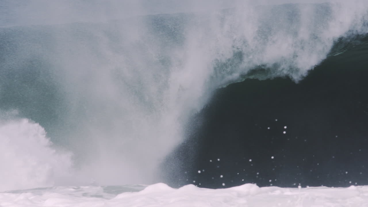 Midday wave bursts in sunlight, mist and sea spray flung wide in high contrast, slow motion telephoto