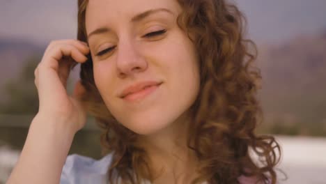 Wind-blows-in-the-curly-red-hair-of-a-beautiful-young-woman,-camera-dolly-in