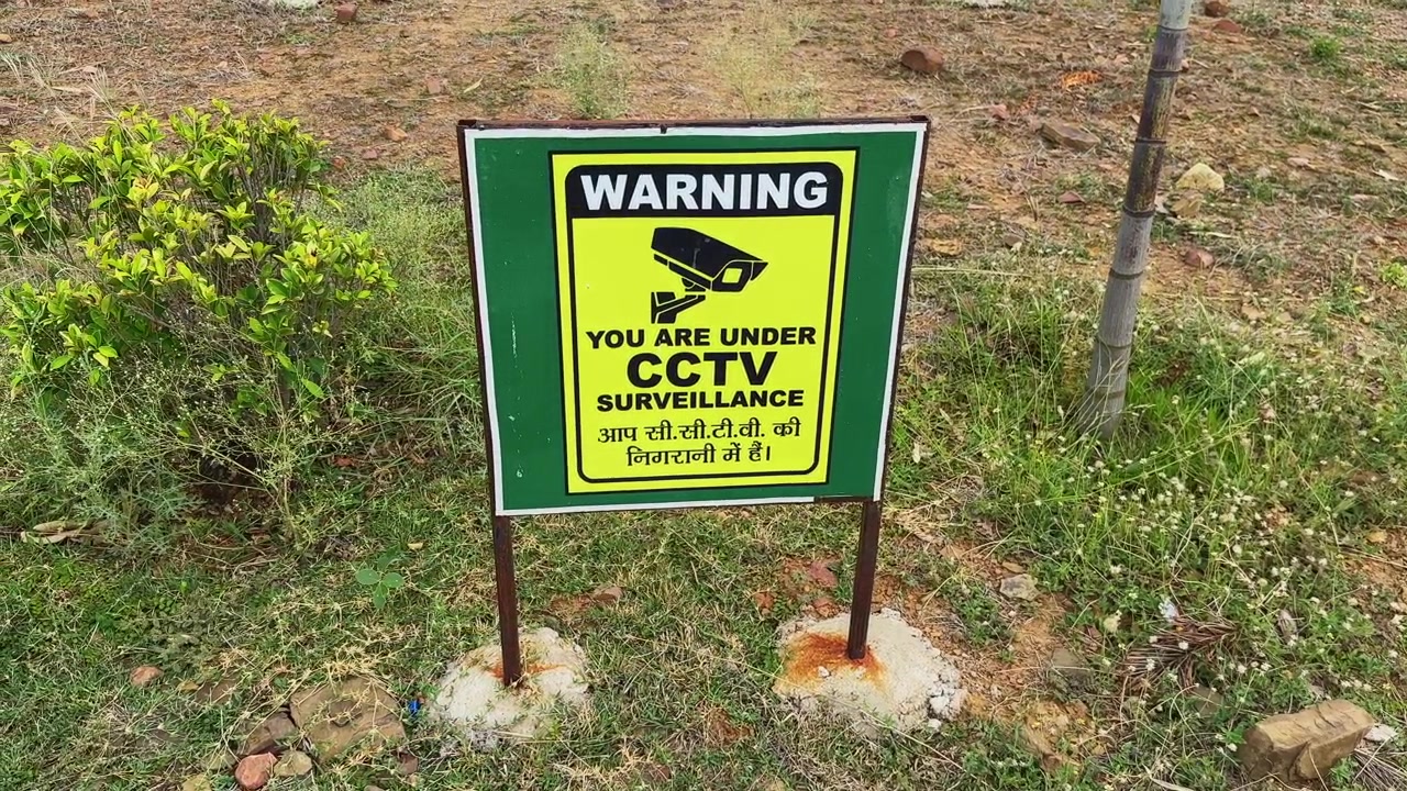Camera orbiting around a CCTV surveillance warning sign installed outdoors highlighting public security monitoring in a landscaped open environment