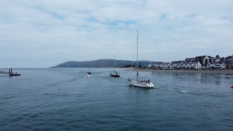 Aerial-orbiting-view-following-sailing-boats-travelling-scenic-Welsh-village-river-estuary