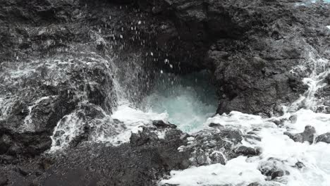 Powerful-ocean-waves-hitting-hole-in-rocky-cliff-making-splash,-static-view