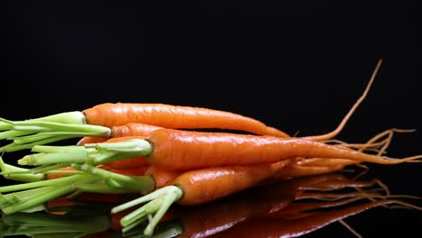 a bundle of baby carrots rotates on a glossy black surface, highlighting their vibrant color and fresh appearance