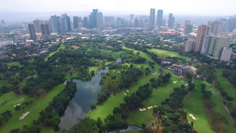 Weit-Ausziehbare-Luftaufnahme-Des-Golfplatzes-Mit-Spiegelung-Des-Himmels-Vom-Teich-Und-Der-Skyline-Der-Stadt-Im-Hintergrund