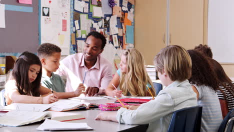 Lehrer,-Der-Mit-Grundschulkindern-An-Ihrem-Schreibtisch-Arbeitet-Working