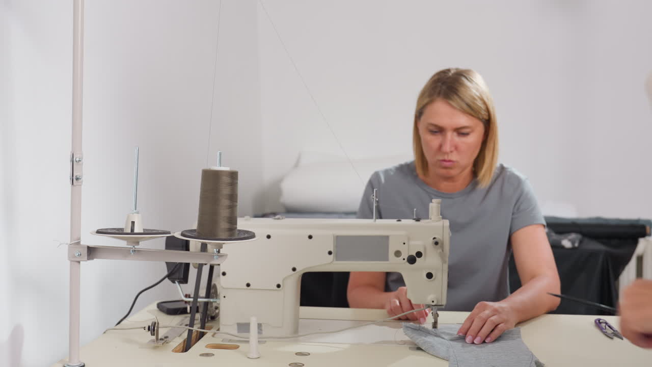 Two dress makers collaborating on industrial sewing machine with brown thread spool, adjusting settings, demonstrating teamwork, craftsmanship, shared expertise in garment production environment