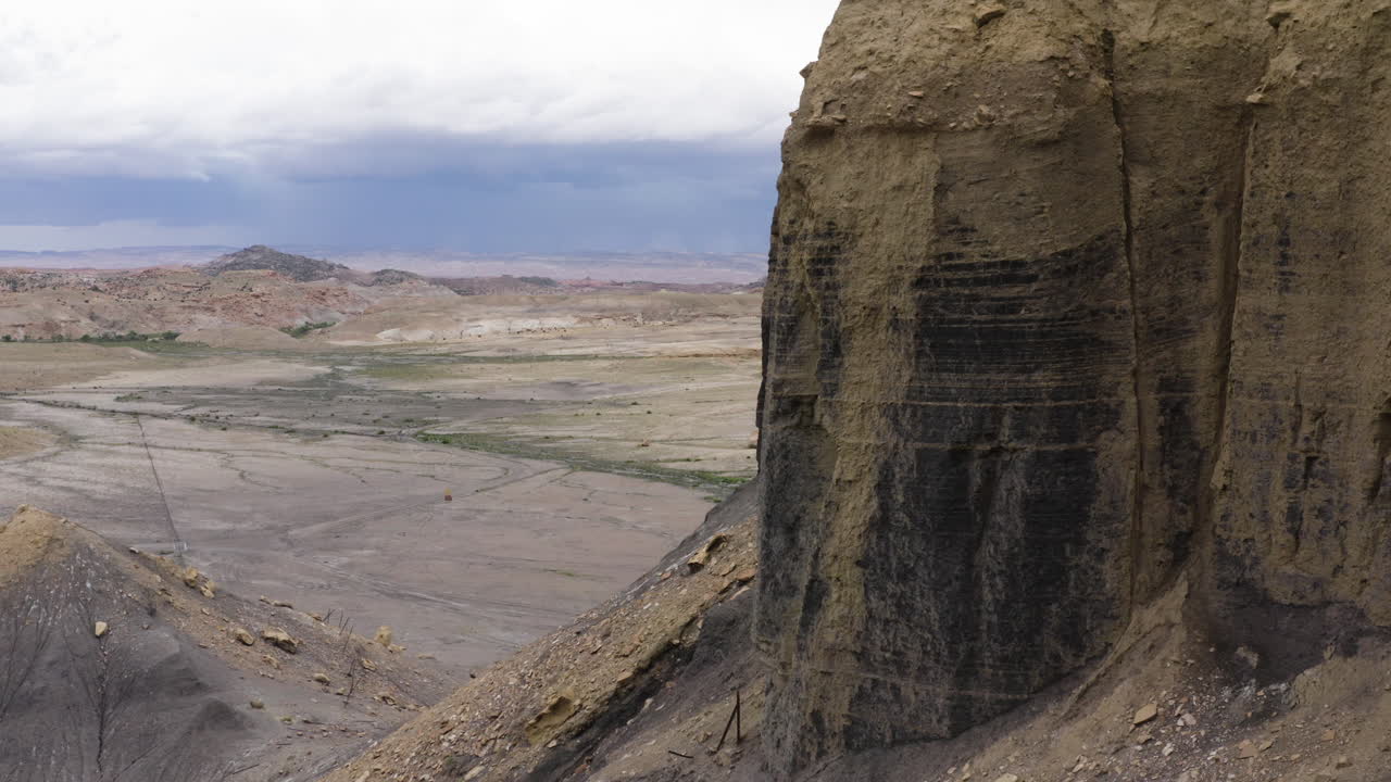 vista aérea de una colina elevada en moab, utah, con un vasto paisaje de desierto y cañón en el fondo, mostrando el terreno accidentado y dramático bajo un cielo nublado