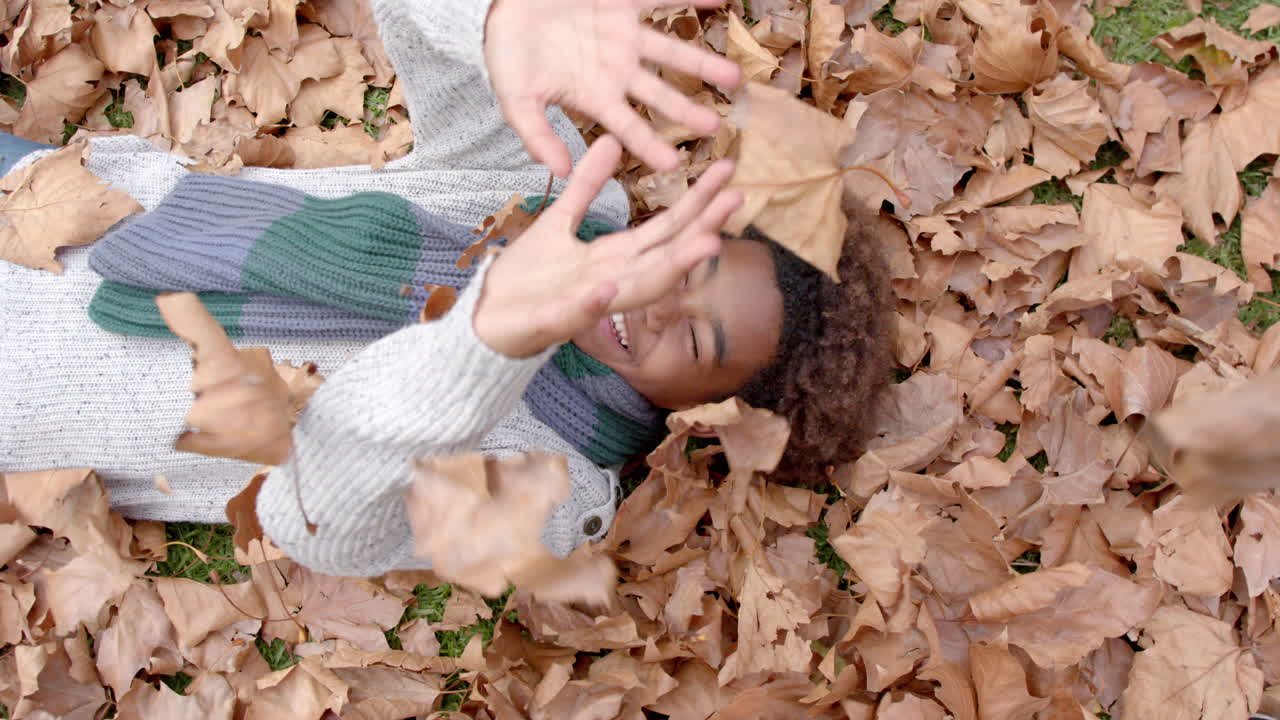 Happy african american boy playing with leaves in garden, in slow motion