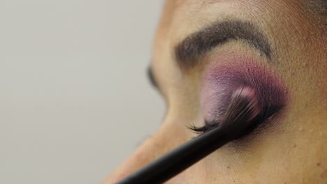 woman applies purple eye shadow on eyelid with fluffy brush, close-up
