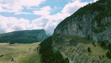 Along-impressive-rock-wall-with-green-pines,-Mount-Granier,-French-Alps