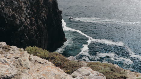 Motor-Boat-moving-by-cliffs-at-Cabo-de-São-Vicente-on-Algarve-shot-from-cliff-in-slow-motion