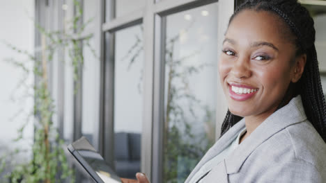 Portrait-of-happy-african-american-casual-businesswoman-using-tablet-in-office-lounge,-slow-motion