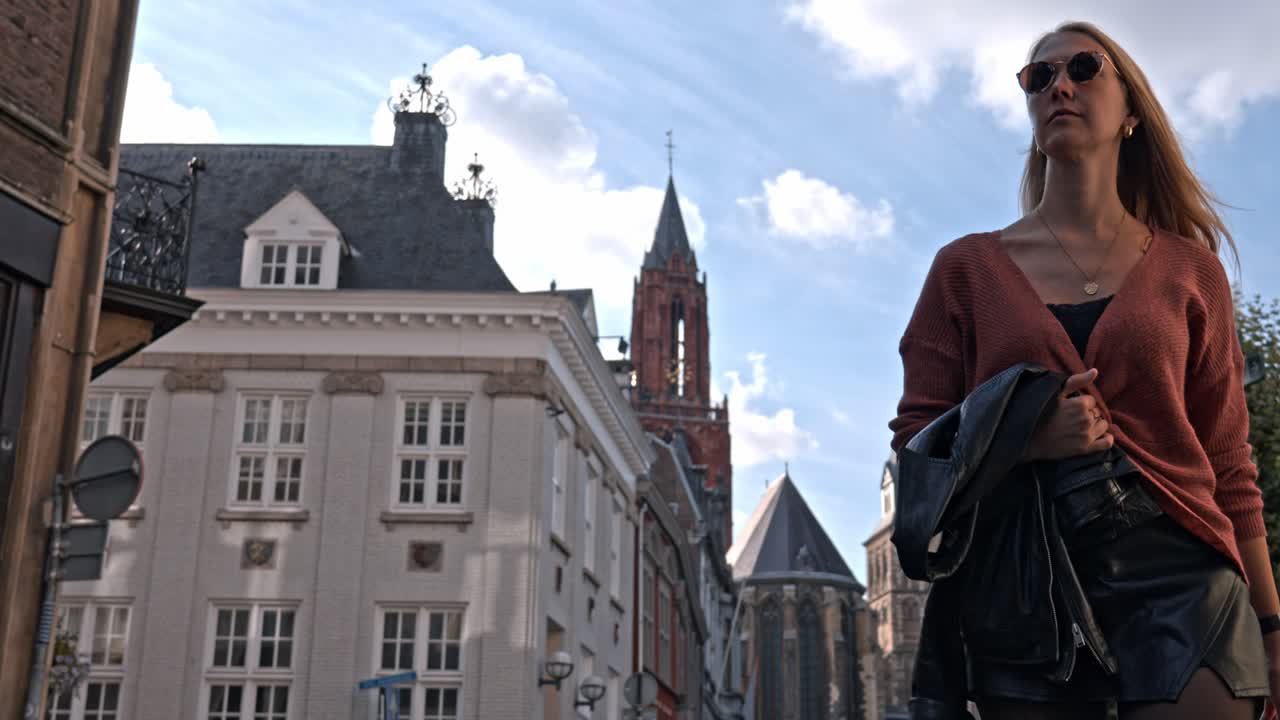 Woman on Vrijthof square in a sunny day, the historic center of Maastricht, Netherlands. The background is dominated by the iconic red tower of the Sint-Janskerk (St. John's Church)