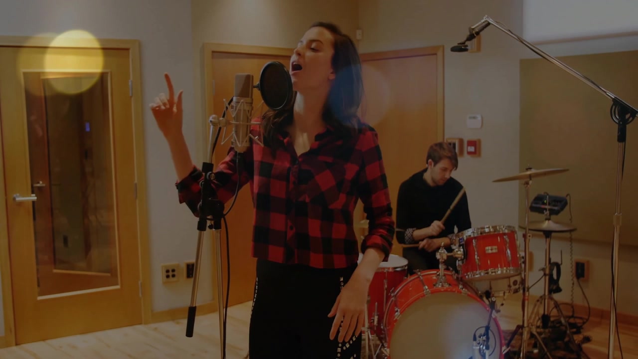 Cantante donna che si avvicina al microfono e canta dolcemente per la produzione musicale mentre il batterista suona.
