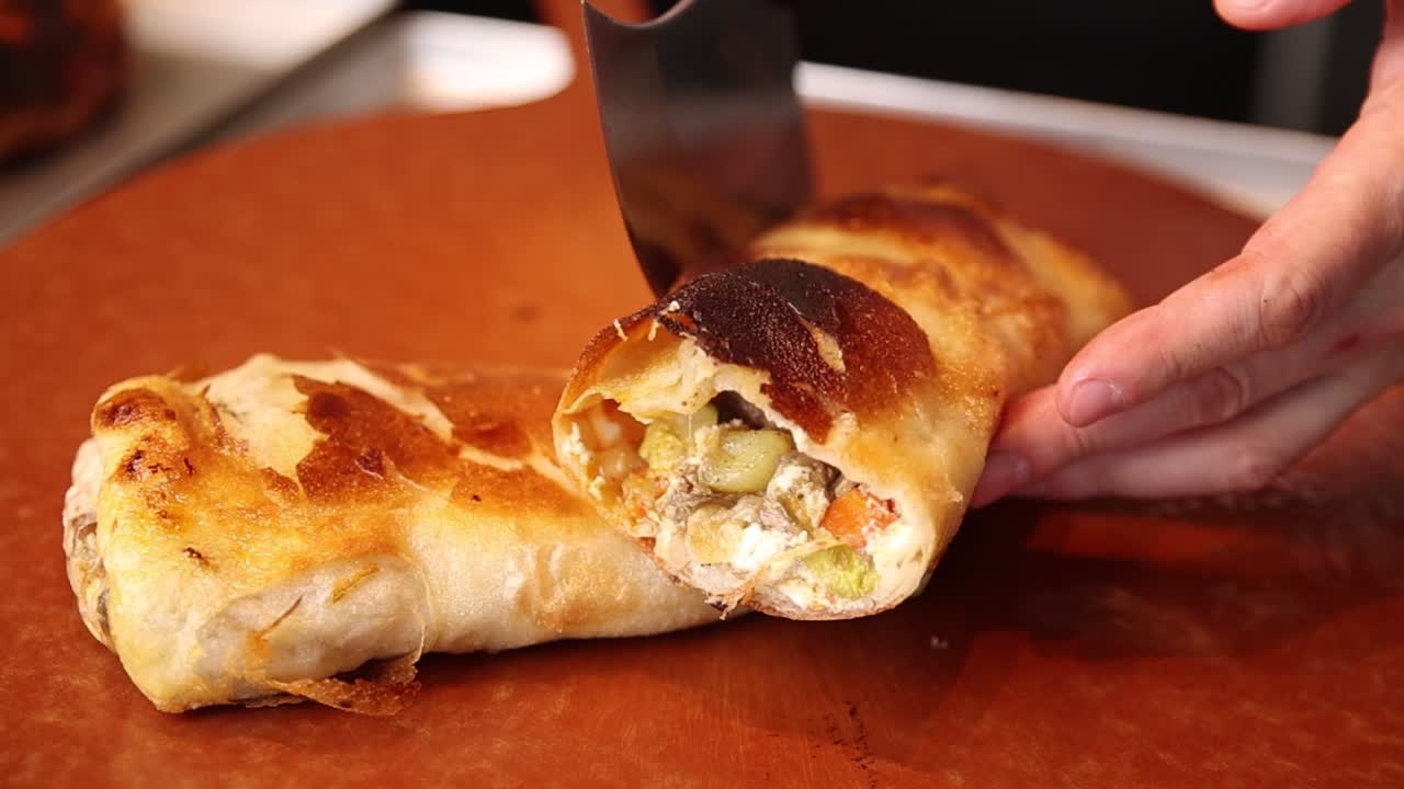 Primo piano di una mano che taglia un rotolo di pasta salata con ripieno di carne e verdure