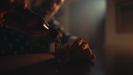 slow motion shot of man pouring alcohol in a glass cup from a bottle with blurred background