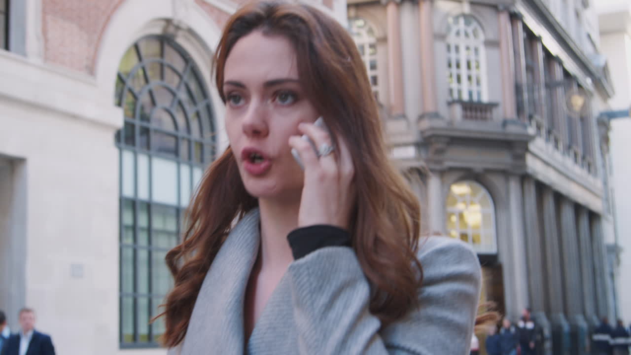 Primo piano di una donna d'affari millennial elegantemente vestita che cammina per strada e parla al suo smartphone, con messa a fuoco sul primo piano.