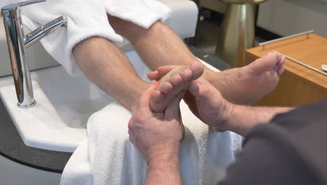 foot massage, masseur massaging the sole of a man at nail lounge and salon