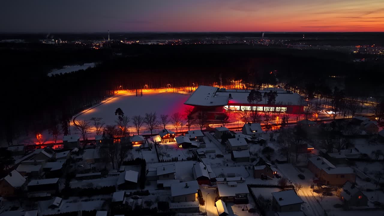 Lumipeitteinen alue, jossa kirkkaasti valaistu rakennus ja taloja päivän päätteeksi auringonlaskun aikaan.
