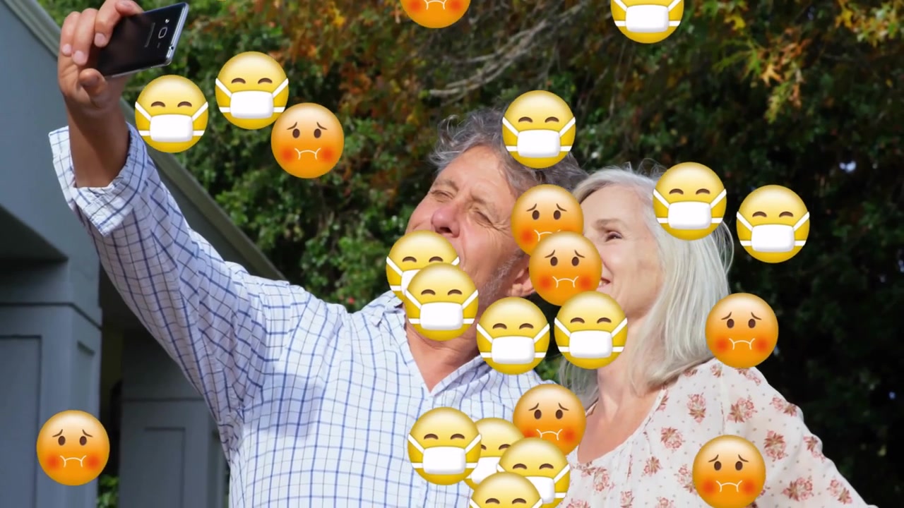 Senior couple raising smartphone for selfie on social media outside house, with emojis floating