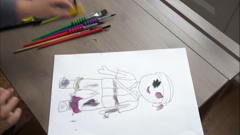 An-over-the-shoulder,-mid-shot,-timelapse-of-a-small-boy-colouring-in-pirate-figures-with-watercolours,-sat-inside-at-a-desk