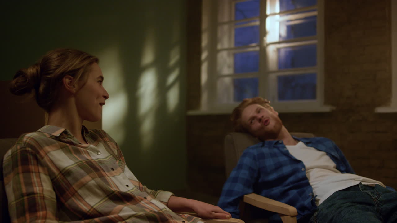 기쁜 커플이 의자에 앉아 있다. 여자가 집에 있는 남자에게 다리를  ⁇ 고 있다.