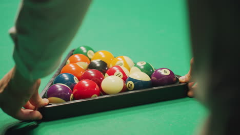 close-up back shot of hand in white shirt gently rolling a well-arranged set of colorful billiard balls in triangle formation on green pool table. the precise setup highlights focus, and preparation