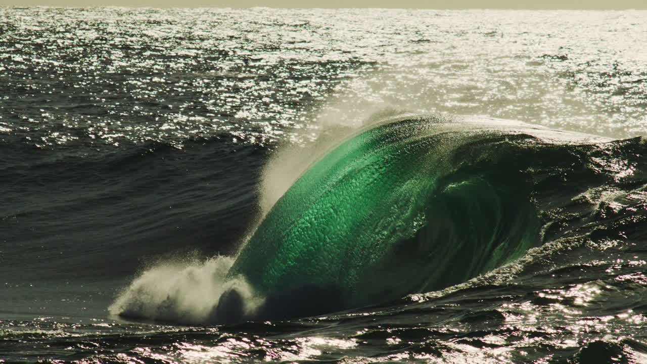 Barreling wave breaks hard with mist swirling in air and textured ripple catching sunlight