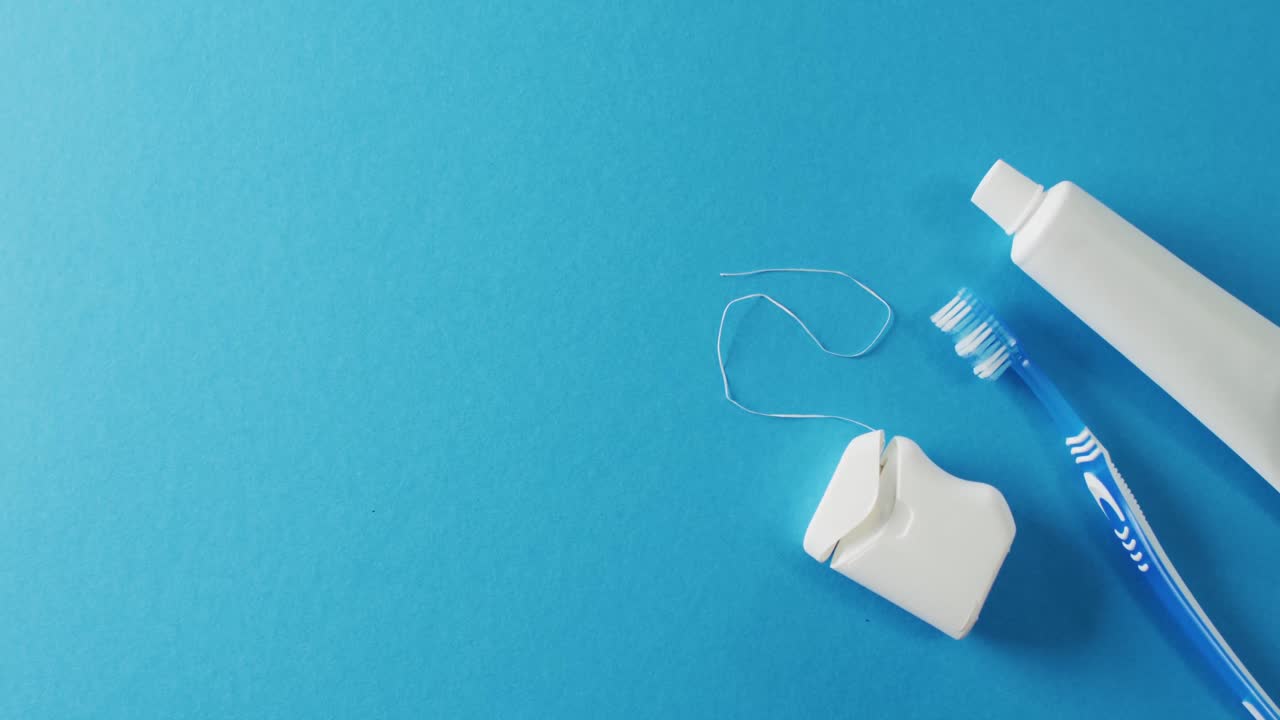 Video of close up of toothbrush, paste and floss on blue background