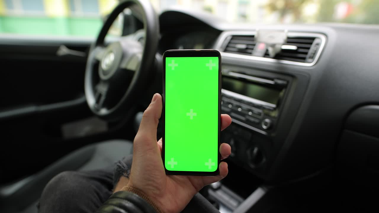 mano masculina sosteniendo la pantalla verde vacía del teléfono inteligente en el coche