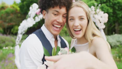 portrait of happy diverse couple holding hands with ring on sunny day at wedding