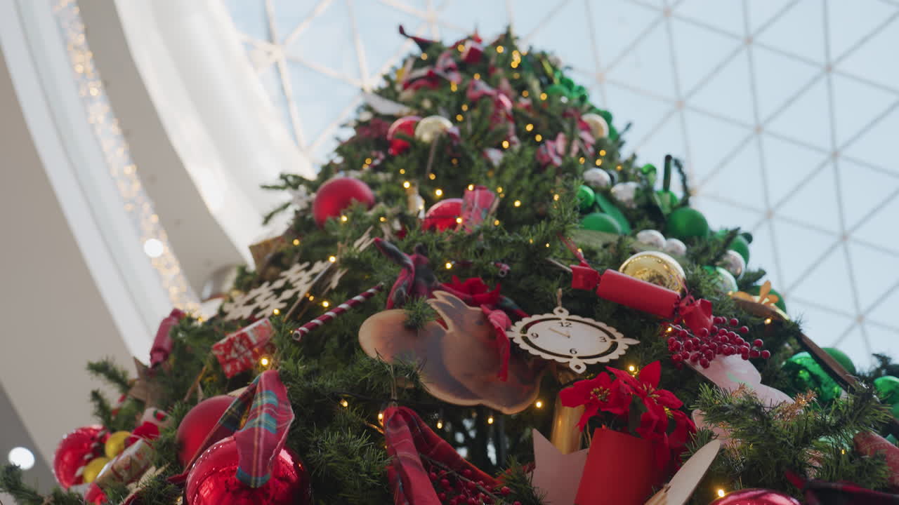 Close-up of beautifully decorated Christmas tree with glowing lights, red and gold ornaments, Santa figurine, gift boxes, and festive decorations creating a warm holiday atmosphere