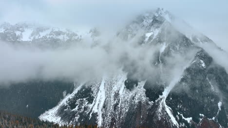 enormous mountain coated with fog in the mount rainer national park, washington state, the usa. drone footage above the snowy pine-trees covering the area.